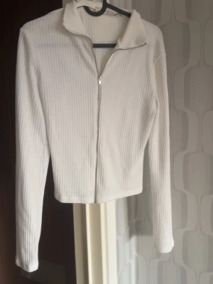 Vit ribbad ziptröja med krage -  en vit ribbad ziptröja med krage och långa ärmar. Lite genomskinlig, använd mycket men inget som är synligt. Mycket tretchig i, ganska tunn (så du vet den passar kanske inte som kofta)