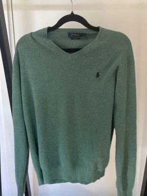 Grön v-ringad tröja från Polo Ralph Lauren - Snygg grön v-ringad tröja från Polo Ralph Lauren med klassisk broderad logga på bröstet. Tröjan har långa ärmar och ribbade muddar vid ärmslut och nederkant. Perfekt för lager-på-lager och enkel att matcha med jeans eller chinos. Storlek s och xs