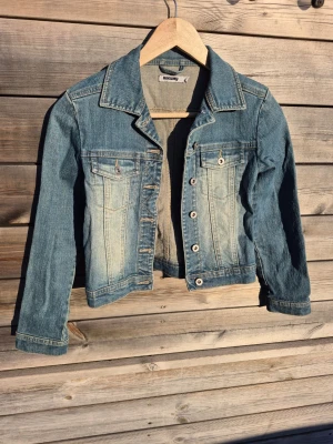 Blå jeansjacka - Blå jeansjacka med klassisk krage, bröstfickor med lock och knappar framtill.