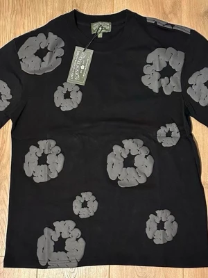 Svart t-shirt med gråa blommor - Cool svart t-shirt från A Bathing Ape med gråa blommönster tryckta över hela tröjan. Klassisk passform och rund halsringning. Perfekt för dig som vill sticka ut med en unik streetwear-look.