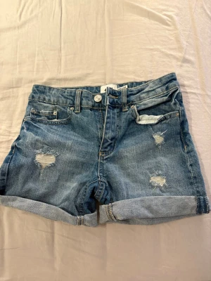 Blå denimshorts med slitningar - Blåa shorts med lite hål i. Det finns så man kan justera storleken i midjan. 