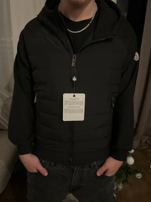 Svart pufferjacka från Moncler - Säljer en svart pufferjacka från Moncler med huva och dragkedja framtill. Jackan har Moncler-logga på vänster ärm och två sidofickor med dragkedja. Materialet är en mix av vadderad front och mjuka ärmar, perfekt just nu när våren kommit!