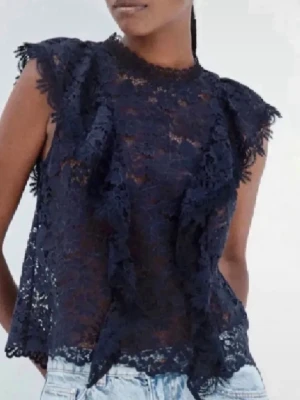 Mörkblå spetsblus med volang - Supersnygg mörkblå blus i spets med volangdetaljer framtill och längs ärmhålen. Ärmlös modell med rund halsringning och transparent material som ger en cool look. Perfekt att styla med jeans eller kjol för en trendig outfit.