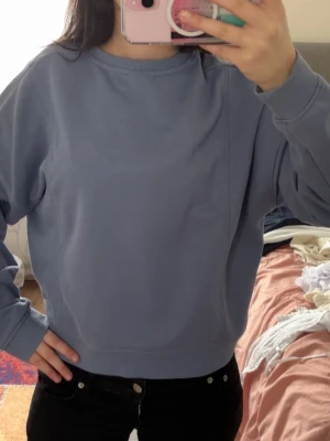 Ljusblå sweatshirt med rund hals - En stilren ljusblå sweatshirt med rund halsringning och ribbade muddar vid ärmslut och nederkant. Tröjan har en avslappnad passform och är tillverkad i mjukt bomullsmaterial. Perfekt för en chill och enkel look.