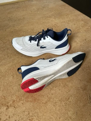 🐊 Lacoste Run Spin 0721 - Fint skick! - Säljer mina Lacoste Run Spin i klassiskt vitt och marinblått. Skorna är använda en del men har tagits väl om hand och är fortfarande i bra skick (se bilder för egen bedömning av sulan och tyget). Mycket bekväma och lätta sneakers som har mycket kvar att ge! • Storlek: 41 (UK 7.5 / USA 8.5) • Skick: Bra begagnat skick. • Originalbox ingår! 