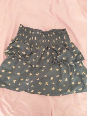 Blommig blå kjol från lager 157 - Supersöt blå kortkjol från lager 157  med små blommor.  Kjolen har volangdetalj upptill och är perfekt för dig som gillar en romantisk stil. Lätt och luftig, passar perfekt till varmare dagar. Har använts sällan.