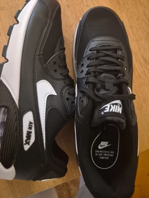 Nike Air Max svart vita sneakers - Snygga Nike Air Max sneakers i svart med vita detaljer och logga. Skorna har en klassisk låg siluett, tjock vit sula. Perfekta för dig som gillar streetwear och sportig stil.