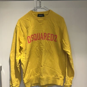 Gul sweatshirt från DSQUARED2 - Gul sweatshirt från DSQUARED2 med röd logotyp framtill. Tröjan har rund halsringning, långa ärmar och ribbade muddar vid ärmslut och nederkant. Perfekt för en avslappnad och trendig stil.