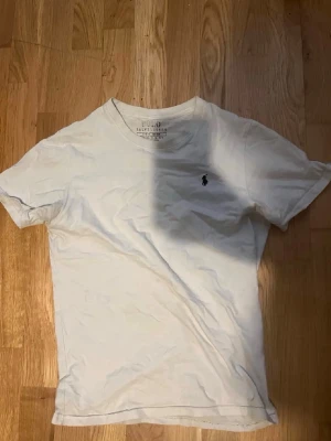 Vit t-shirt från Polo Ralph Lauren - Klassisk vit t-shirt från Polo Ralph Lauren med rund hals och den ikoniska svarta logotypen broderad på bröstet. Tillverkad i mjuk bomull och har en normal passform. Perfekt basplagg för alla tillfällen.
