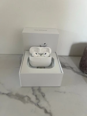 Apple AirPods Pro 2 - Säljer ett par vita Apple AirPods Pro med trådlöst laddningsetui. Hörlurarna har en stilren och kompakt design med silikonproppar för bättre passform. Kommer i originalförpackning. Perfekta för musik, samtal och träning.