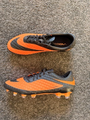 Nike Hypervenom Phantom RGN SE Fg - ⚽️ Nike Hypervenom Phantom RGN SE FG | Strl 42 | HELT NYA ⚽️  Säljer ett par Nike Hypervenom Phantom RGN SE FG i svart/orange. Helt nya och aldrig använda.  ✅ Storlek: 42 ✅ Skick skor: Nya / oanvända ✅ FG (gräs) ✅ Skopåse medföljer (använd men i bra skick, se bilder)  🔥 Eftertraktad och svår att få tag på modell.  📦 Skickas snabbt. 📸 Se bilder för detaljer och skick. 