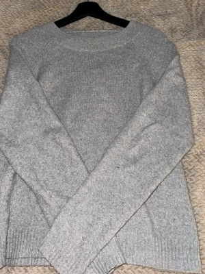 Grå stickad tröja från Vero Moda - Mysig grå stickad tröja från Vero Moda med rund halsringning och långa ärmar. Tröjan har en enkel och stilren design med ribbade muddar vid ärmslut och nederkant. Perfekt att matcha med jeans eller kjol.