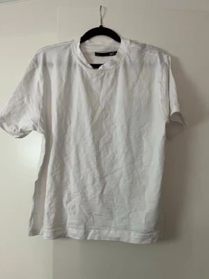 Vit t-shirt från 157, storlek M - En klassisk vit t-shirt från 157 i storlek M. T-shirten har rund halsringning och korta ärmar, perfekt för en enkel och clean look. Tillverkad i mjuk bomull som känns skön mot huden.