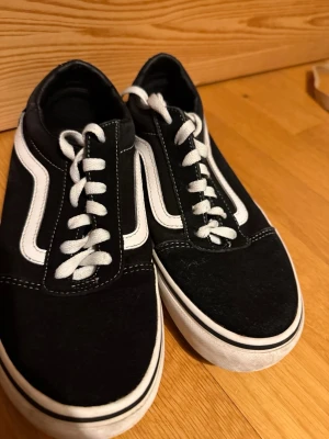 Svarta Vans sneakers - Klassiska Vans Old School sneakers i svart med vit sula och vita sidostripes. Skorna har låga skaft, vita snören och kontrastsömmar. 