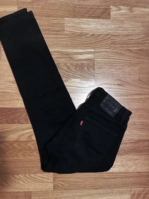 Svarta Levi’s 512 jeans slim fit - Svarta Levi's 512 jeans med slim passform och klassisk femficksdesign. Jeansen har en snygg svart läderpatch bak och Levi's röda etikett på bakfickan. Perfekt för dig som gillar stilrena och tajta jeans.