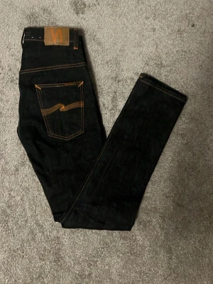 Nudie jeans  - Tja säljer nu dem här snygga och stilrena jeansen från Nudie! Storlek L32, W30! Skick 9/10! Färg mörkgrå/blå med lite orangea detaljer! Pris endast 319kr! Hör av er vid minsta lilla fråga eller fundering! 