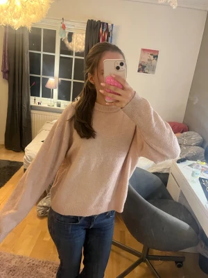 Ljusrosa stickad tröja med rund hals - Mysig ljusrosa stickad tröja med rund hals och långa ärmar. Tröjan har en enkel design med ribbstickade muddar vid hals, ärmslut och nederkant. Perfekt för att hålla sig varm under kyliga dagar.