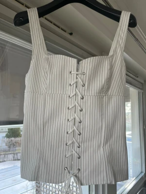 Vit randig korsettopp med snörning - Trendig vit korsettopp från Zara. Knytning fram och dragkedja bak. Svår att få tag på. Storlek S.