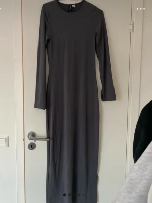 Grå långärmad långklänning H&M - En stilren grå långklänning från H&M med lång ärm och rund halsringning. Klänningen har en rak och enkel passform som sitter snyggt längs kroppen. Perfekt för dig som gillar minimalistisk stil.
