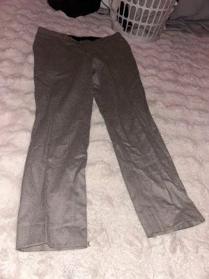 Grå kostymbyxor med rak passform - Snygga grå kostymbyxor med klassisk rak passform och diskreta fickor bak. Materialet är tunt och känns mjukt, perfekt för dig som vill ha en stilren look. Passar dig som gillar enkel och tidlös design.