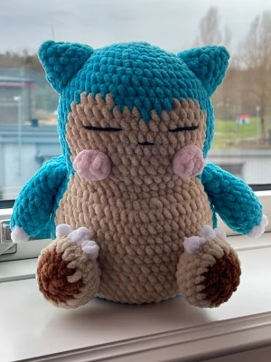 Virkat Snorlax gosedjur - Handgjort virkat Snorlax gosedjur i mjukt sammetsgarn. Färgerna är turkos/blå, beige, brun och rosa. Figurerad kropp med små öron, stängda ögon och söta rosa kinder. En uppskattad figur bland barn som mysig maskot.