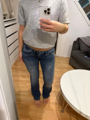 Blå bootcut jeans med slitningar - Ny annons med fri frakt!!! Snygga blå bootcut jeans med lätt slitna detaljer på låren och klassisk femficksdesign. Jeansen har låg midja och dragkedjegylf. Perfekta för en avslappnad och trendig look.