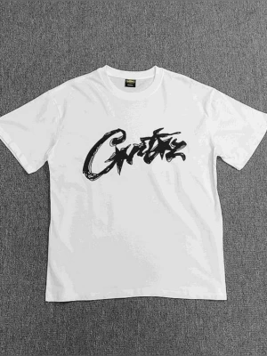 Vit t-shirt med svart graffiti-tryck - Snygg vit t-shirt från Crusty med ett stort svart graffiti-inspirerat tryck på bröstet. Klassisk rund hals och korta ärmar. Perfekt för dig som gillar streetwear och vill sticka ut med en unik design.