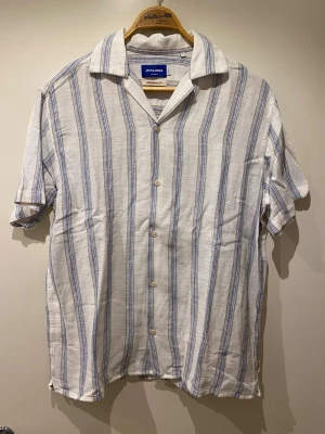 Randig skjorta från Jack & Jones - Säljer en vit skjorta från Jack & Jones med blåa vertikala ränder. Aldrig använt (fel storlek och glömde returnera). Storlek L. Nypris 499kr. 