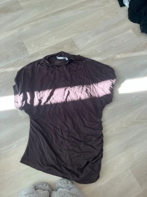 Brun kortärmad t-shirt - Säljer en enkel brun t-shirt från lager med rund hals och korta ärmar. Perfekt för dig som gillar basic plagg med relaxed vibe. Materialet känns mjukt och lätt, perfekt att matcha med jeans eller shorts.