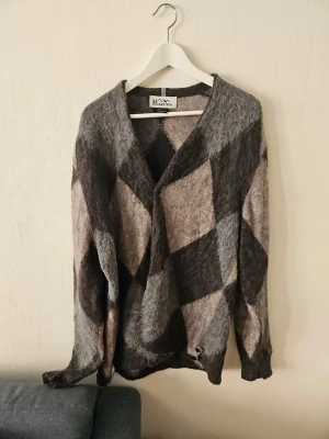 Gråbrun rutig kofta från Manastash - Säljer en oversized kofta från Manastash i mjuk, lurvig ullblandning. Koftan har ett stort rutmönster i olika nyanser av grått och brunt, med djup v-ringning och långa ärmar. Perfekt för lager-på-lager och chill stil.