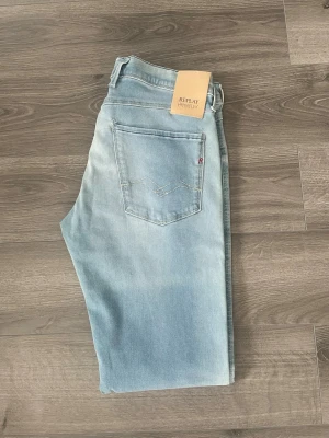 Ljusblå Replay jeans - Snygga ljusblå jeans från Replay med raka ben och klassisk femficksdesign. Jeansen har en diskret tvättad look och är tillverkade i stretchigt denim för extra komfort. Perfekta för en avslappnad och trendig stil. De är i den mest populära modellen Anbass. Storlek 31/32. 