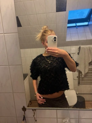 Svart transparent blus med struktur - Säljer en svart transparent blus med cool struktur och mönstrad yta. Blusen har korta ärmar och en lös passform, perfekt att styla med smycken och höga byxor. Materialet känns lätt och luftigt, vilket gör den extra bekväm.