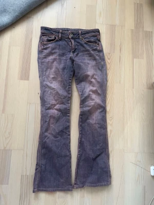 Lågmidjade Bootcut jeans  - Säljer ett par bootcut jeans i lila denim med fem fickor och låg midja. Jeansen har klassisk knappgylf och synliga sömmar i kontrastfärg. Perfekta för dig som gillar retrostil och vill sticka ut med en unik färg på dina jeans.