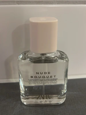 Zara Nude Bouquet parfym - Zara Nude Bouquet är en stilren parfym i en genomskinlig glasflaska med ljusbeige lock. Doften är blommig och fräsch, perfekt för dig som gillar eleganta och moderna parfymer. Flaskan har en enkel och snygg design som passar på vilken hylla som helst.