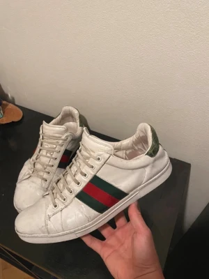 Gucci ace - Klassiska vita sneakers från Gucci med den ikoniska gröna och röda randen på sidan. Skorna har lågt skaft, vita snören och detaljer i grönt på hälen. Tillverkade i läder och har en stilren, tidlös design som passar till det mesta. Går såklart att pruta😁