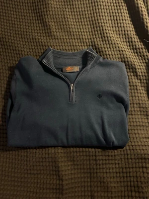 Mörkblå quarter zip från Ralph Lauren - Mörkblå tröja från Ralph Lauren med quarter zip och liten broderad logga på bröstet. Tröjan har ribbade muddar vid ärmslut och nederkant samt hög krage. Perfekt för en stilren och avslappnad look.