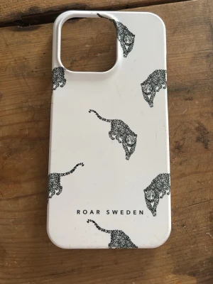 Vitt mobilskal med leoparder Roar Sweden - Snyggt vitt mobilskal från Roar Sweden med svartmönstrade leoparder. Skalets form är anpassad för iPhone 13 Pro och har en stor öppning för kameran. Tillverkat i hårdplast som skyddar mobilen och ger en stilren look.