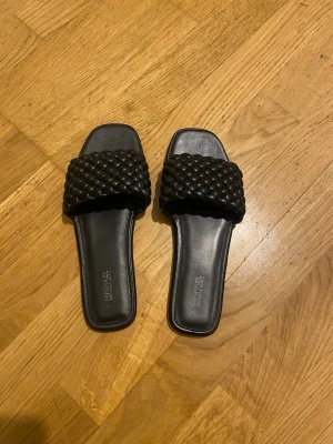 Svarta flätade sandaler Michael Kors - Säljer ett par svarta sandaler från Michael Kors med bred, flätad rem och fyrkantig tå. Perfekta för dig som vill ha en trendig och enkel look.