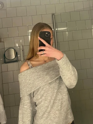 Ljusgrå off shoulder stickad tröja - Trendig ljusgrå stickad tröja med bred off shoulder-krage. Mjuk och skön. Långa ärmar och avslappnad passform ger en chill vibe. Passar perfekt till jeans eller kjol för en snygg look. Säljer den då den inte kommer till användning längre, kontakta mig om ni har några frågor💞