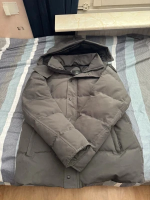 Canada goose wyndham parka puffer - Säljer en mörkgrå pufferjacka med stor huva och dragkedja samt knappar framtill. Jackan har två stora fickor på sidorna och en patch på ärmen. Perfekt för kalla vinterdagar och riktigt skön att bära.                                                                XXL Men Det känns som L storlek.