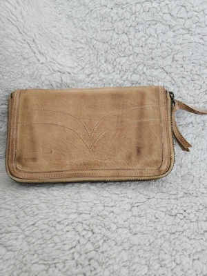 Beige senapsgul plånbok i äkta läder - Snygg beige plånbok i äkta läder med dragkedja runtom och dekorativa sömmar på framsidan. Baksidan har ett extra fack med dragkedja och läderdetalj. Perfekt storlek för kort, kontanter och mynt.