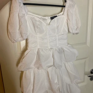Vit klänning från PrettyLittleThing - Säljer en söt vit klänning från PrettyLittleThing med puffärmar och volanger, perfekt till studenten bland annat, går att pruta vid snabb affär 