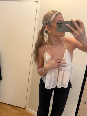 Vit ärmlös linnetopp med volang - Säljer en söt och luftig vit linnetopp med tunna axelband och volangdetalj. Toppen är ärmlös och har en flowy passform som ger en avslappnad och trendig look. Perfekt för varma dagar eller att styla lager på lager.