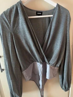 Glittrig body - Snygg glittrig silverfärgad body från Bubbleroom med lång ärm och slitsdetalj på ärmarna. Perfekt för festliga tillfällen!