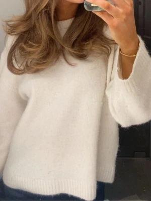 Vit stickad tröja med rund hals - Mysig vit stickad tröja med rund hals och långa ärmar. Tröjan har en enkel, rak passform och ribbstickade muddar vid ärmslut och nederkant. Perfekt för lager på lager och en clean look.