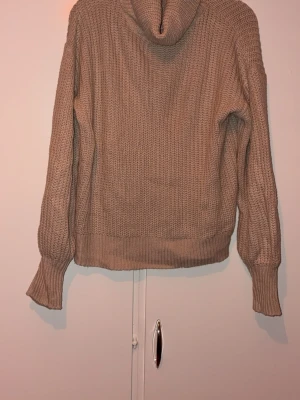 Beige stickad polotröja - Mysig beige stickad polotröja med grovstickad struktur och långa ärmar. Tröjan har breda muddar vid ärmslut och nederkant samt en hög polokrage. Perfekt för kyliga dagar och enkel att matcha med olika outfits.