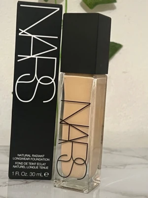 NARS Natural Radiant Foundation in shade Gobi - NARS Natural Radiant Longwear Foundation i en snygg glasflaska med svart lock. Foundationen har en ljus beige ton och ger ett naturligt glow. Förpackningen är stilren med tydlig logga och rymmer 30 ml.
