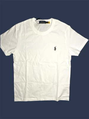 Vit t-shirt från Polo Ralph Lauren - Klassisk vit t-shirt från Polo Ralph Lauren med rund halsringning och den ikoniska broderade loggan på bröstet. Priset kan diskuteras vid snabb affär. Tillverkad i mjuk bomull och har en normal passform. Perfekt basplagg för alla tillfällen.👍