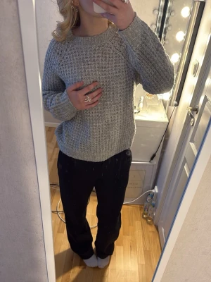 Ljusgrå stickad tröja - Mysig ljusgrå stickad tröja med rund hals och avslappnad passform. Tröjan har ett diskret mönster i stickningen och ribbade muddar vid ärmslut och nederkant. Perfekt för lager på lager och enkel att matcha med olika stilar.