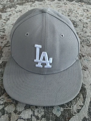 Grå LA Dodgers keps - Snygg grå keps från New Era med LA Dodgers-logga broderad i vitt framtill. Klassisk flat brim och ventilerande hål.